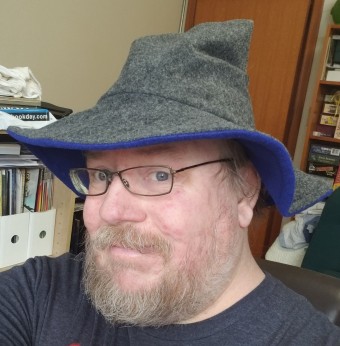 The author, Brent, a large blonde beardy man with glasses, wearing a grey wizard's hat.